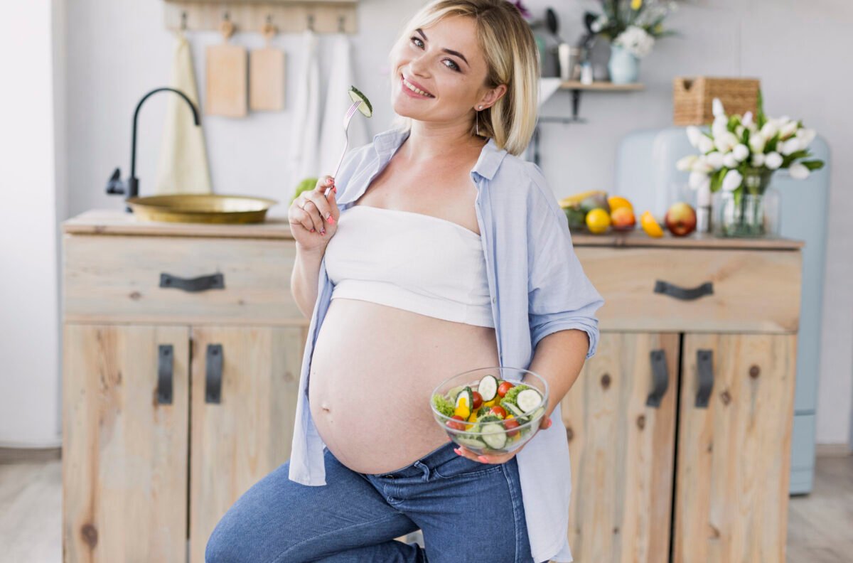 pregnant woman eating salad while looking at the camera